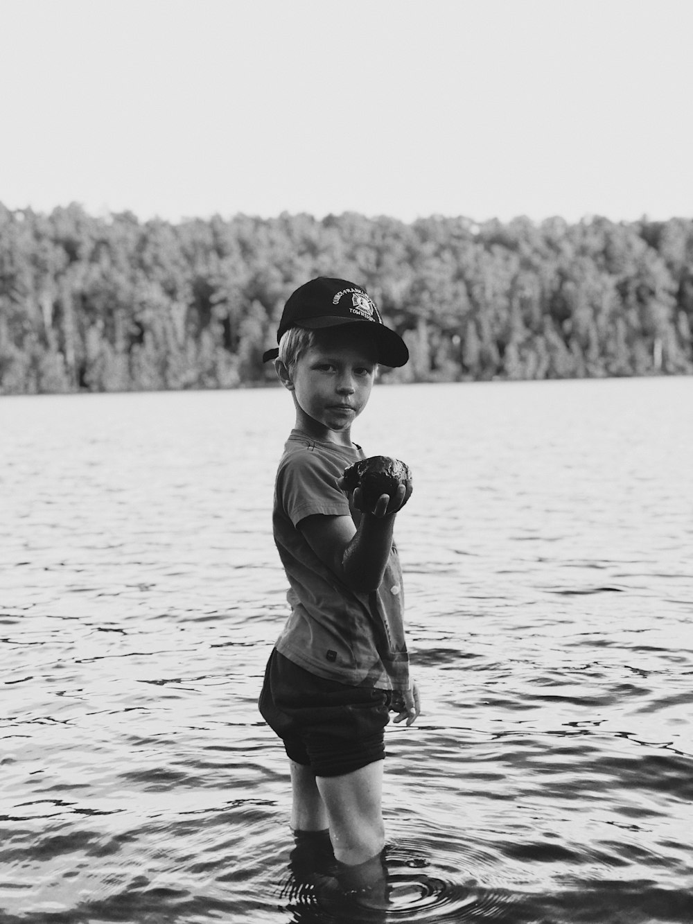 grayscale photo of boy in tank top and shorts holding a ball