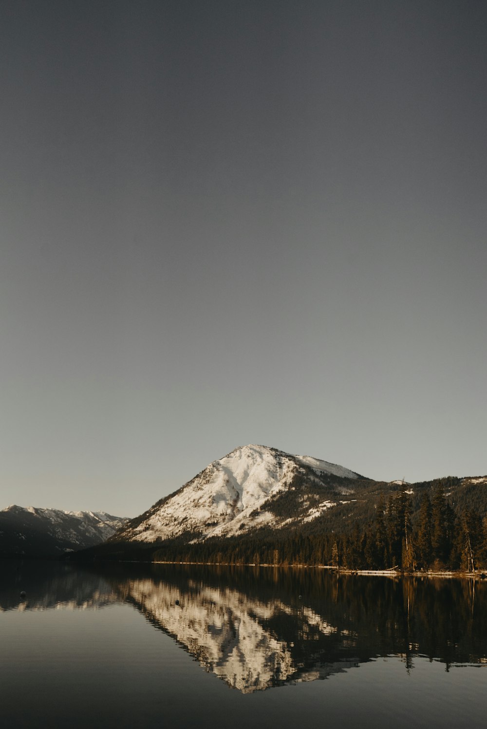 灰色の空の下で湖の近くの雪に覆われた山