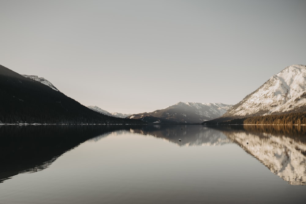 lake near mountain under white sky during daytime