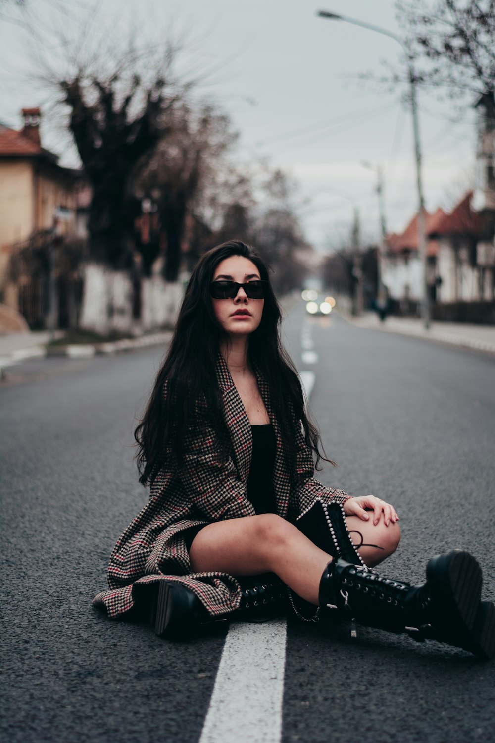 woman in black and white checkered dress shirt and black sunglasses sitting on road during daytime