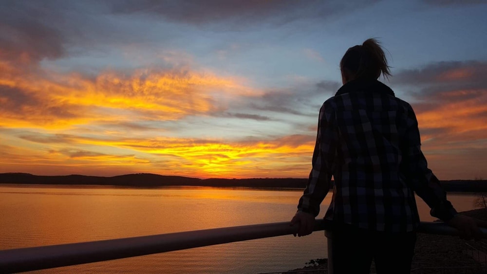 man in black and white plaid dress shirt standing beside railings during sunset