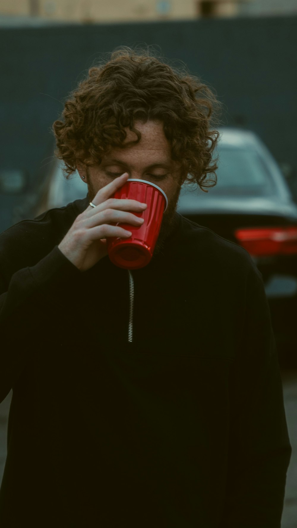 man in black jacket drinking from red ceramic mug
