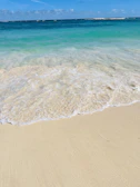 A golden sandy beach with turquoise waves gently rolling under a clear blue sky.
