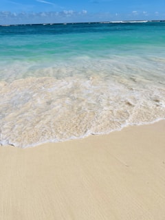 A wide sandy beach with turquoise waves gently rolling in beneath clear skies.