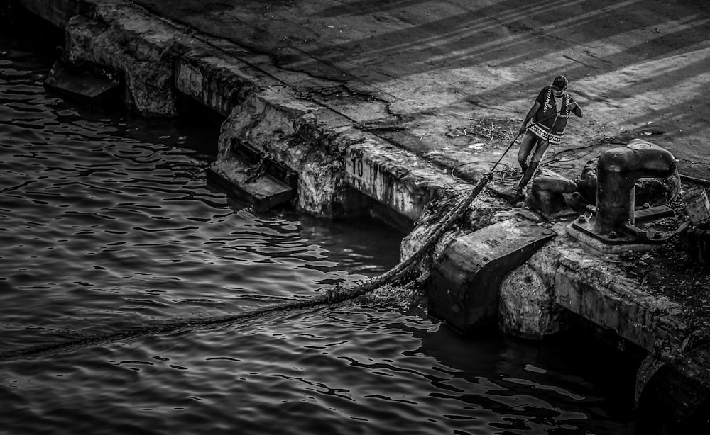 grayscale photo of a man fishing on a river