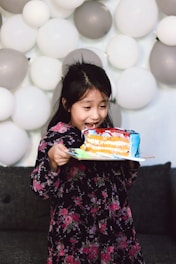 girl in black and pink floral long sleeve shirt holding cake