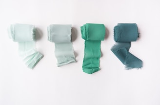 Cuatro rollos de tela verde sobre una superficie blanca, mostrando diversas texturas.