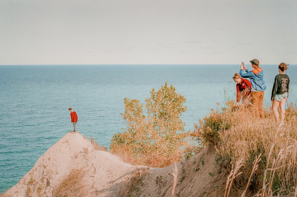 昼間、水辺の茶色の岩の上に立つ赤いドレスを着た女性