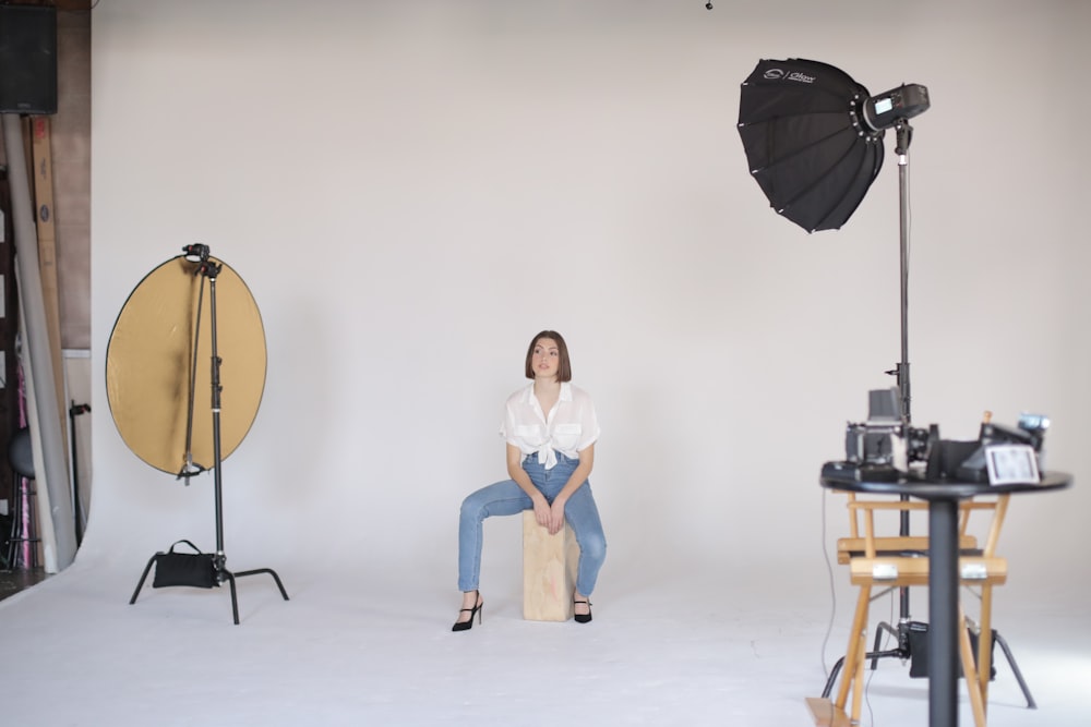 Frau in weißem T-Shirt und blauen Jeansshorts sitzt auf braunem Holzsitz