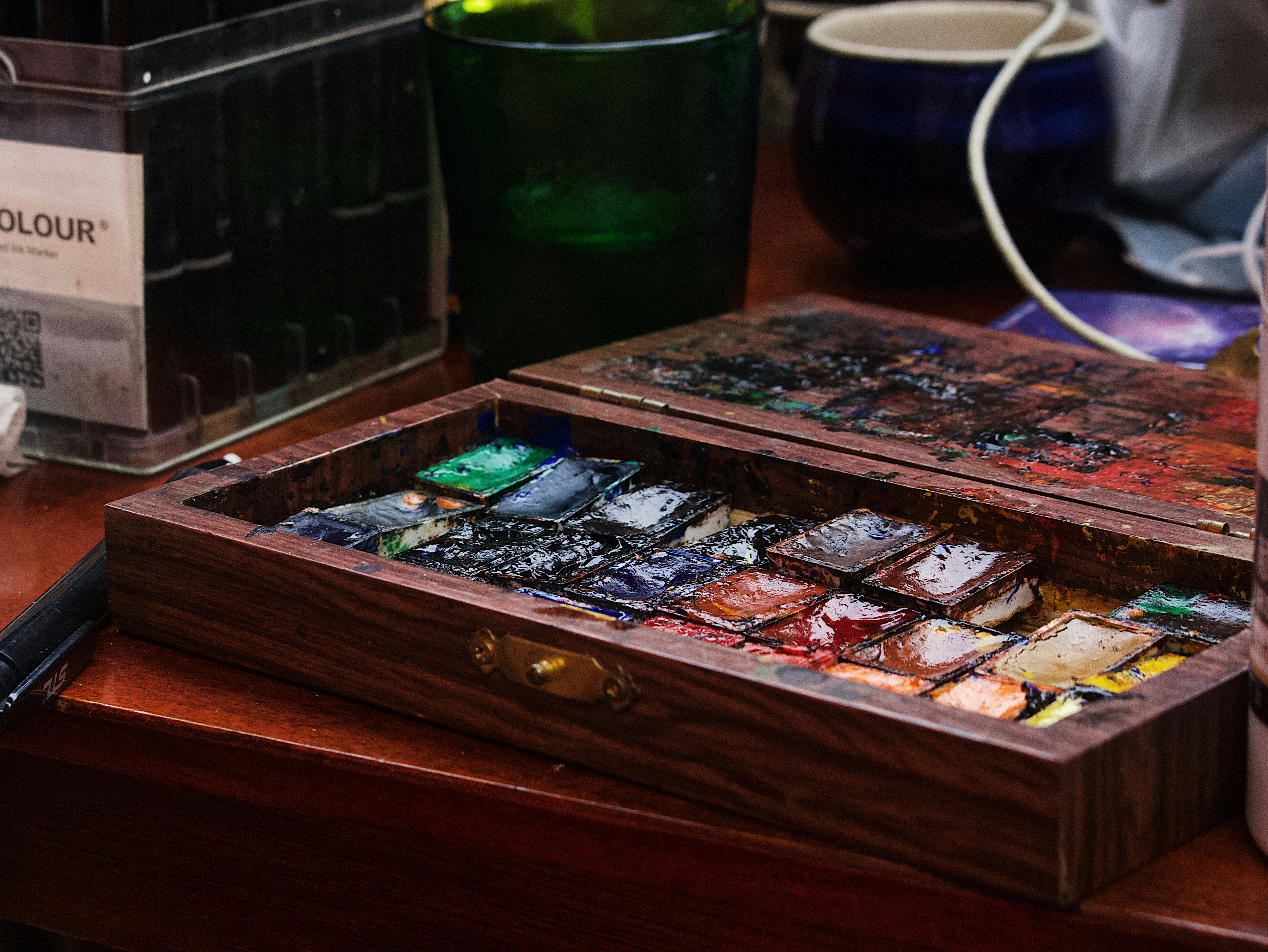Open wooden paint box filled with watercolor pans on a table.