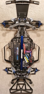 A detailed view of the chassis of a remote-controlled car, showcasing the intricate components like suspension, battery pack, and wiring. The main frame is made of metal and plastic parts, with visible shock absorbers and electronic components neatly arranged.