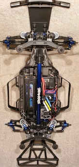 A detailed view of the chassis of a remote-controlled car, showcasing the intricate components like suspension, battery pack, and wiring. The main frame is made of metal and plastic parts, with visible shock absorbers and electronic components neatly arranged.