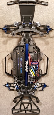 A detailed view of the chassis of a remote-controlled car, showcasing the intricate components like suspension, battery pack, and wiring. The main frame is made of metal and plastic parts, with visible shock absorbers and electronic components neatly arranged.