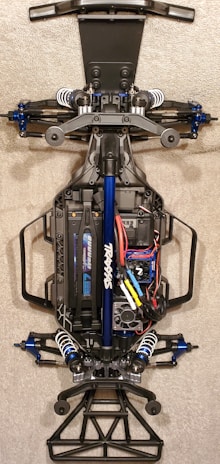 A detailed view of the chassis of a remote-controlled car, showcasing the intricate components like suspension, battery pack, and wiring. The main frame is made of metal and plastic parts, with visible shock absorbers and electronic components neatly arranged.