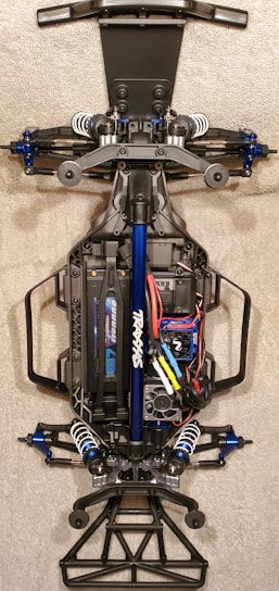 A detailed view of the chassis of a remote-controlled car, showcasing the intricate components like suspension, battery pack, and wiring. The main frame is made of metal and plastic parts, with visible shock absorbers and electronic components neatly arranged.