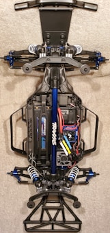 A detailed view of the chassis of a remote-controlled car, showcasing the intricate components like suspension, battery pack, and wiring. The main frame is made of metal and plastic parts, with visible shock absorbers and electronic components neatly arranged.