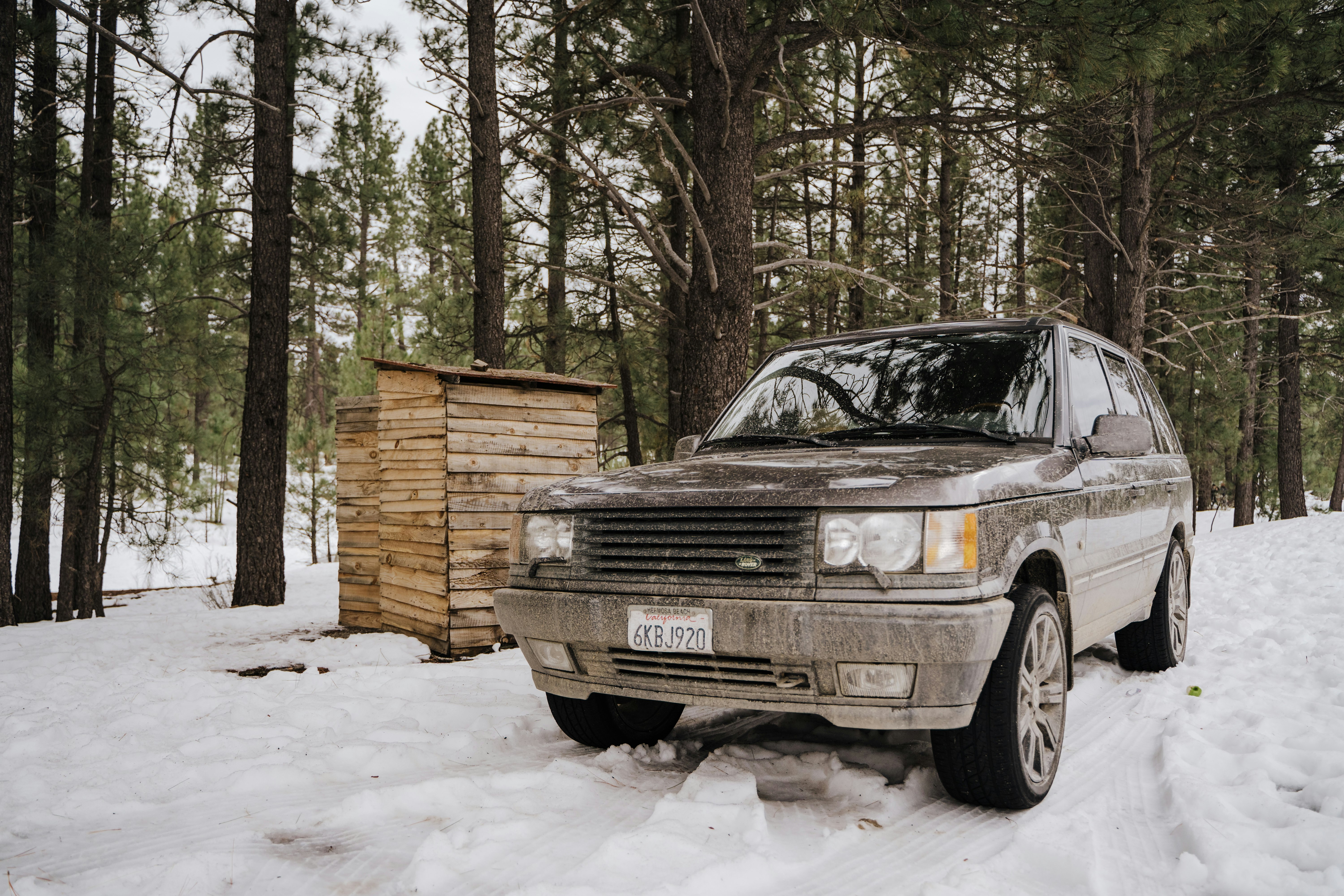 black suv covered with snow near brown wooden house during daytime