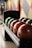 A row of bowling balls of various colors are neatly lined up on a ball rack. The background features a colorful geometric wall design, adding to the vibrant atmosphere typical of a bowling alley.