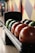 A row of bowling balls of various colors are neatly lined up on a ball rack. The background features a colorful geometric wall design, adding to the vibrant atmosphere typical of a bowling alley.