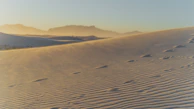 Golden hour light casting long shadows over the desert landscape with distant mountains.