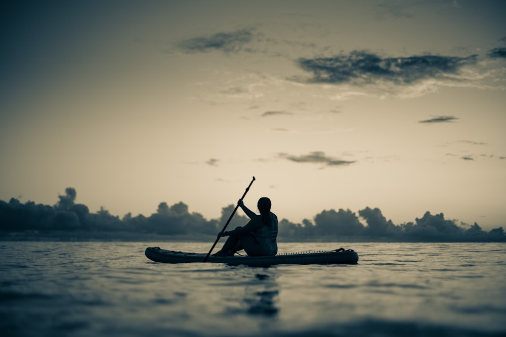 silhouette of man riding on kayak on body of water during daytime