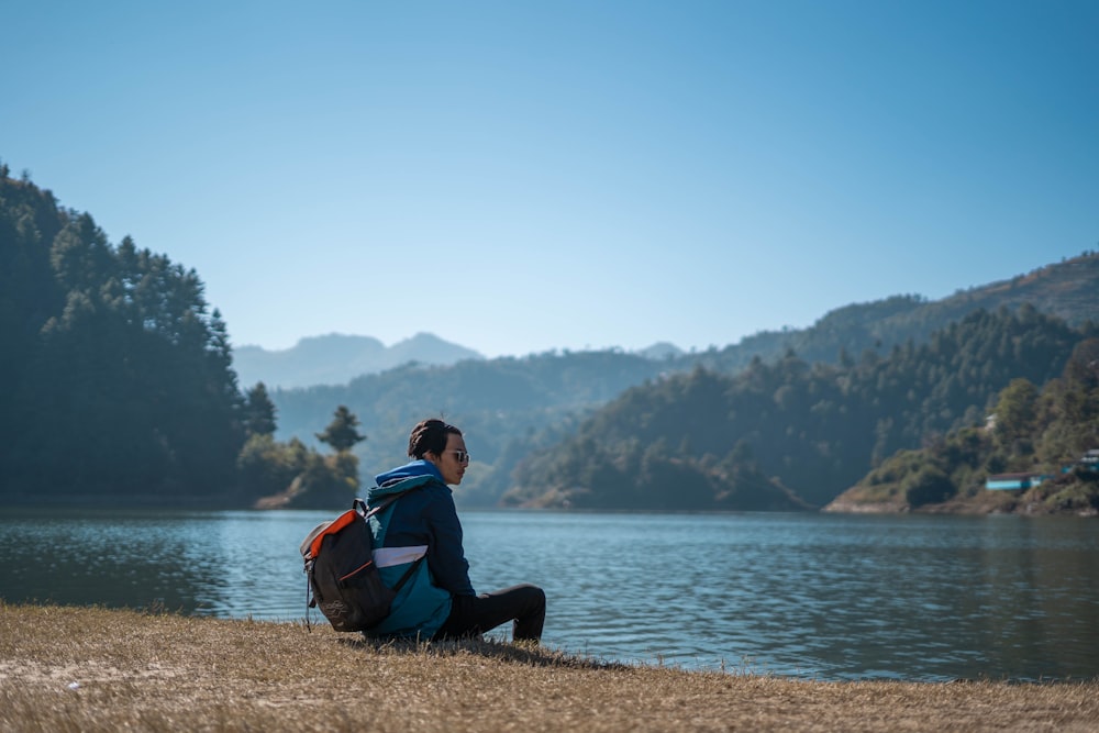 man in black and red jacket sitting on rock near body of water during daytime