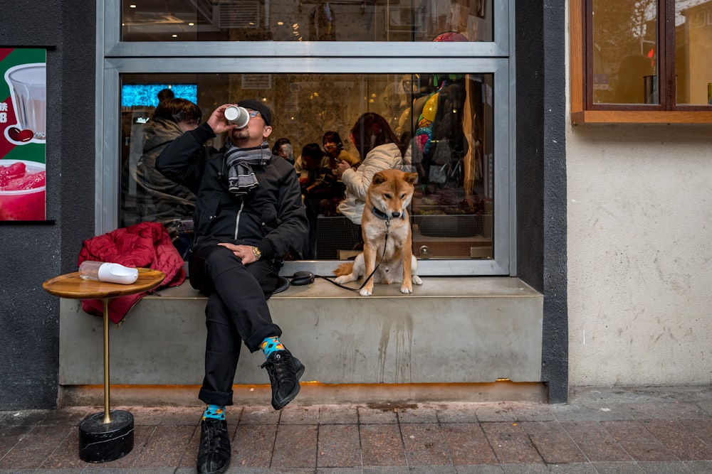 man in black jacket sitting beside brown dog