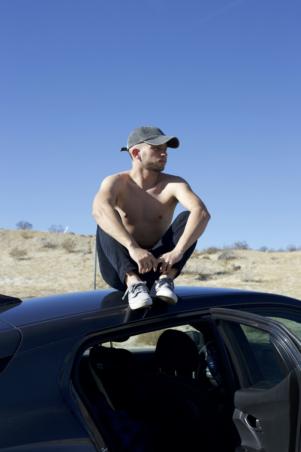 topless man in blue denim jeans and brown cowboy hat sitting on black car during daytime