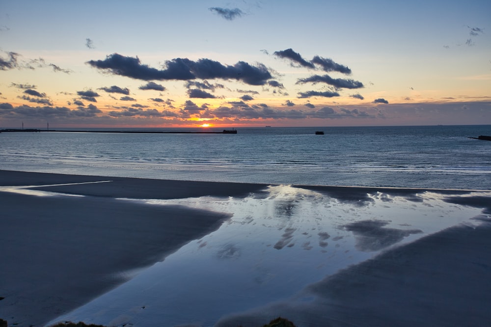 the sun is setting over the water at the beach