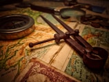A vintage setup consisting of a map, an old-fashioned compass, a pair of dividers, and some coins. The lighting gives a warm, nostalgic feel. The map appears detailed, showing various geographic features and regions. There is also a partial view of a vintage currency note with intricate designs.