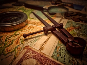 A richly textured close-up of a Victorian-era map with brass compass and quill pen.