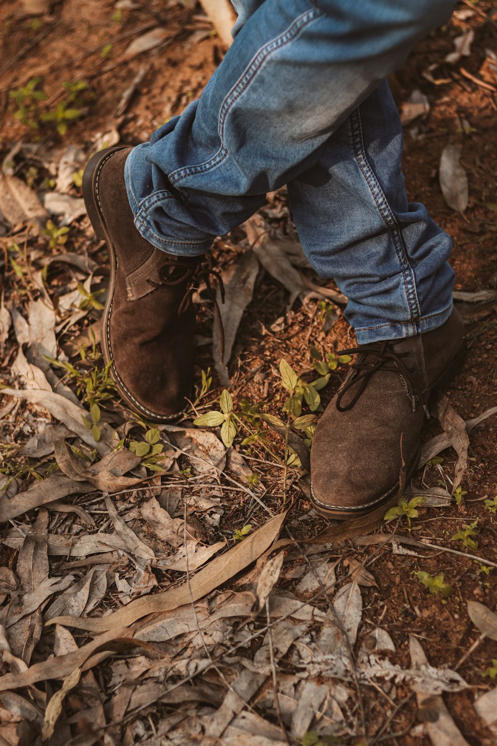 person in blue denim jeans and brown leather boots standing on dried leaves