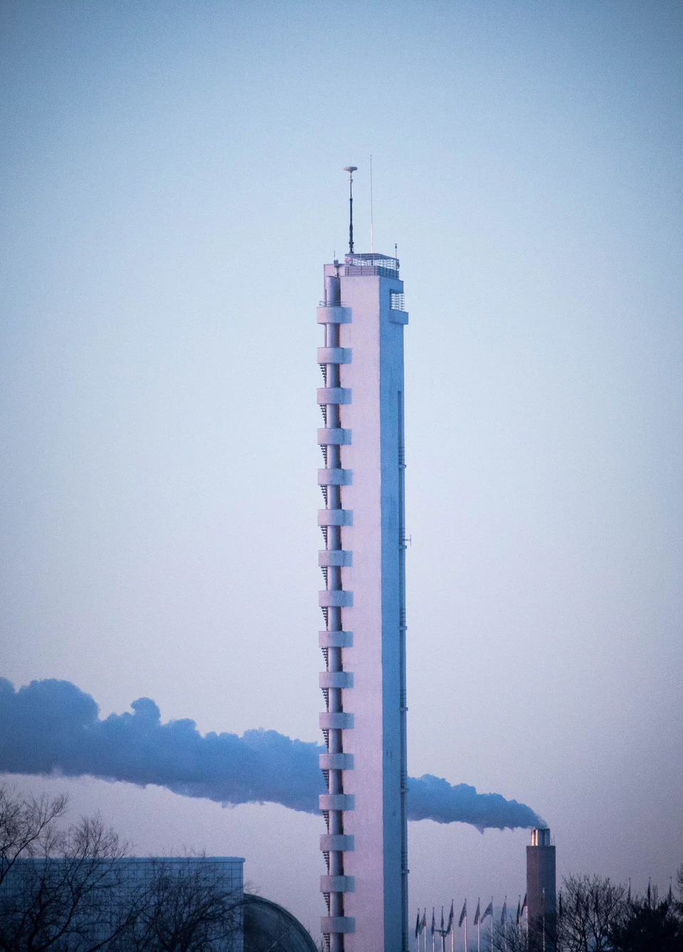 Tall, white tower standing against a clear blue sky with smoke emitting from its chimney