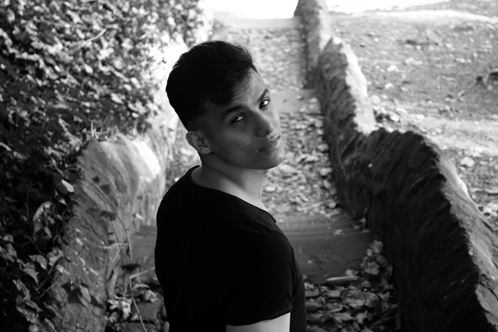 grayscale photo of boy in black shirt standing near rock formation