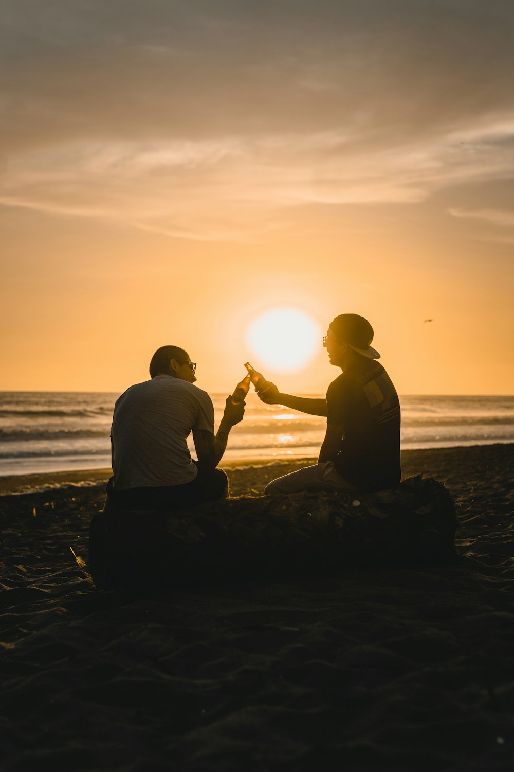 silhouette of 2 men sitting on rock near sea during sunset