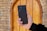 A hand holds a black Samsung smartphone in front of a wooden door set in a brick wall. The phone is being showcased prominently.