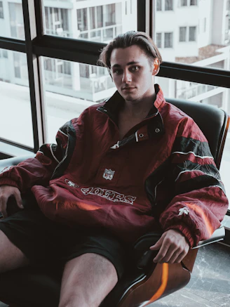 man in red and black zip up jacket sitting on black leather chair