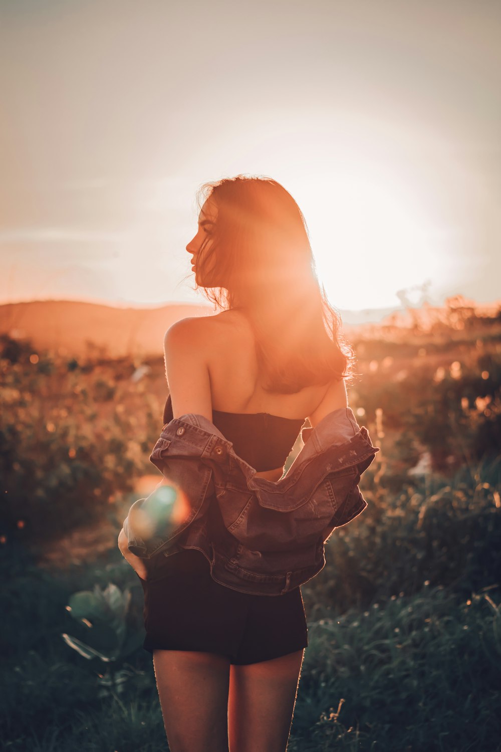 woman in black dress standing on green grass field during sunset