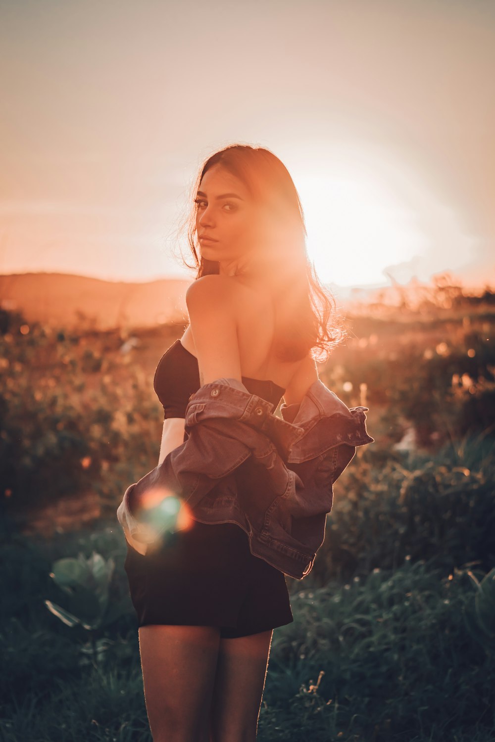 woman in black off shoulder dress standing on green grass field during sunset