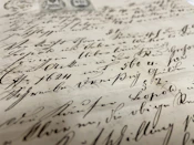A close-up view of an antique manuscript with elegant handwritten text. The ink is dark and appears slightly faded with time, written on aged, yellowed paper. The script is flowing and ornate, indicative of a historical document.