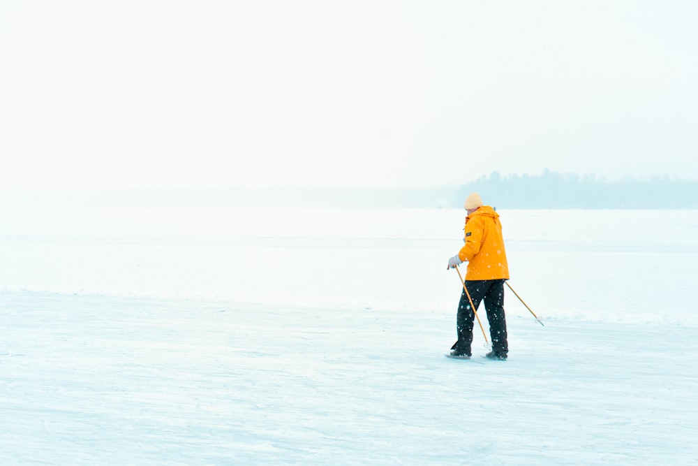 man in yellow jacket and black pants walking on snow covered ground during daytime