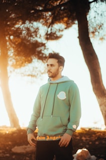 A man wearing a casual t-shirt and hoodie standing outdoors in natural light