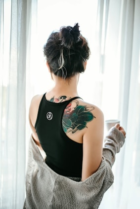 woman in black tank top with green floral tattoo on her back