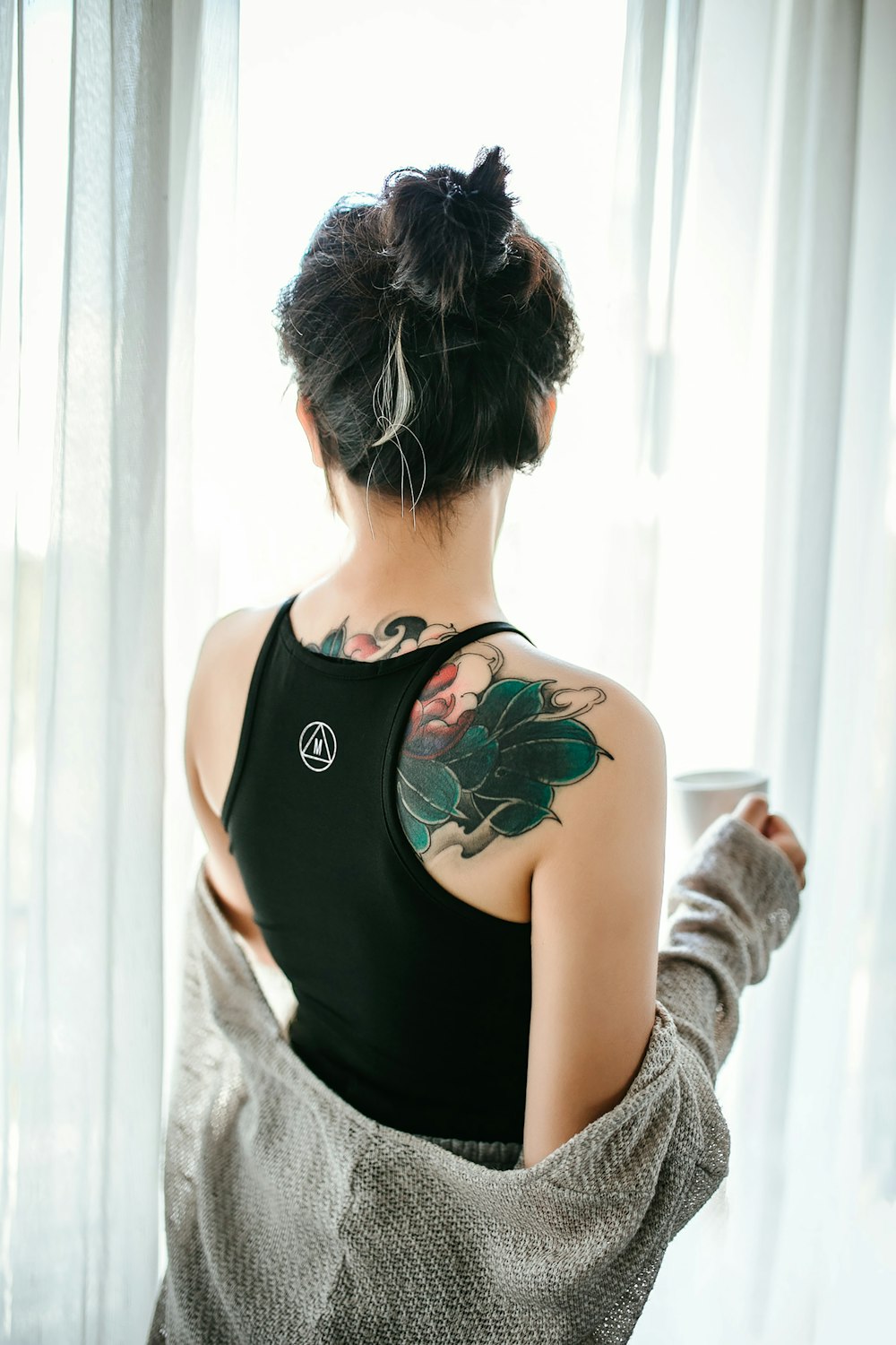 mulher na regata preta com tatuagem floral verde em suas costas