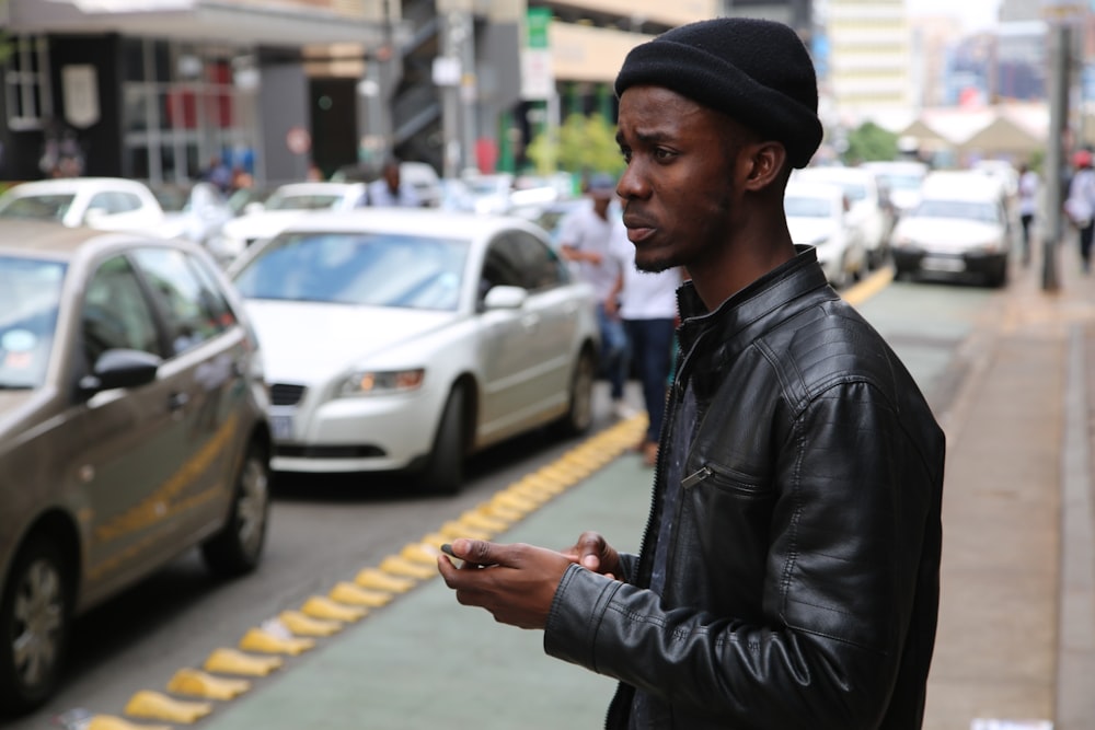 man in black leather jacket standing on sidewalk during daytime