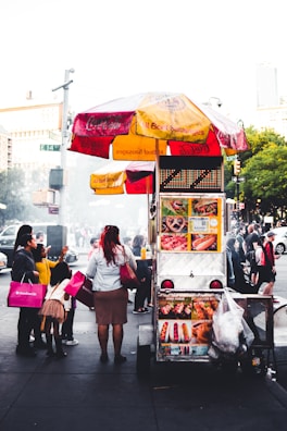 The Nomad Nosh cart parked at a bustling New York street event with happy customers gathered around.