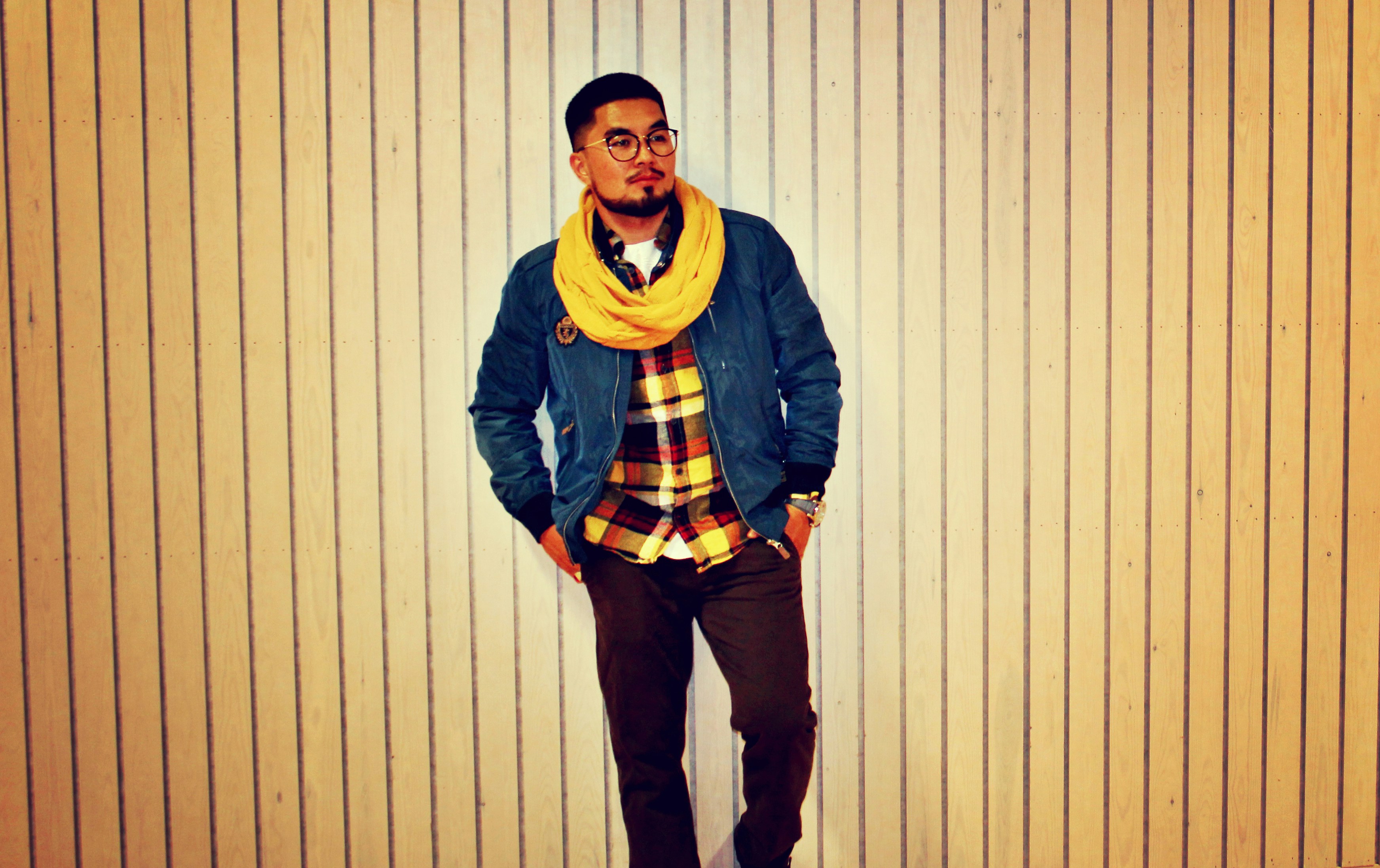 man in blue jacket and yellow scarf standing beside white wall