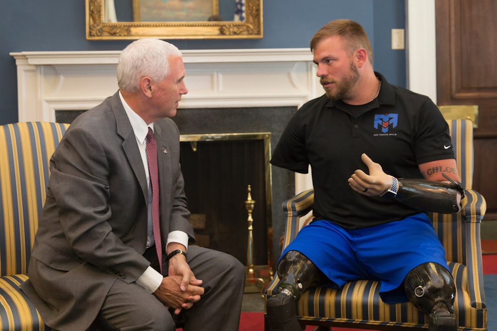 man in black suit sitting beside man in black crew neck t-shirt