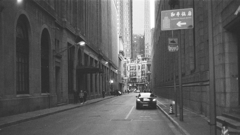 grayscale photo of cars on road between buildings