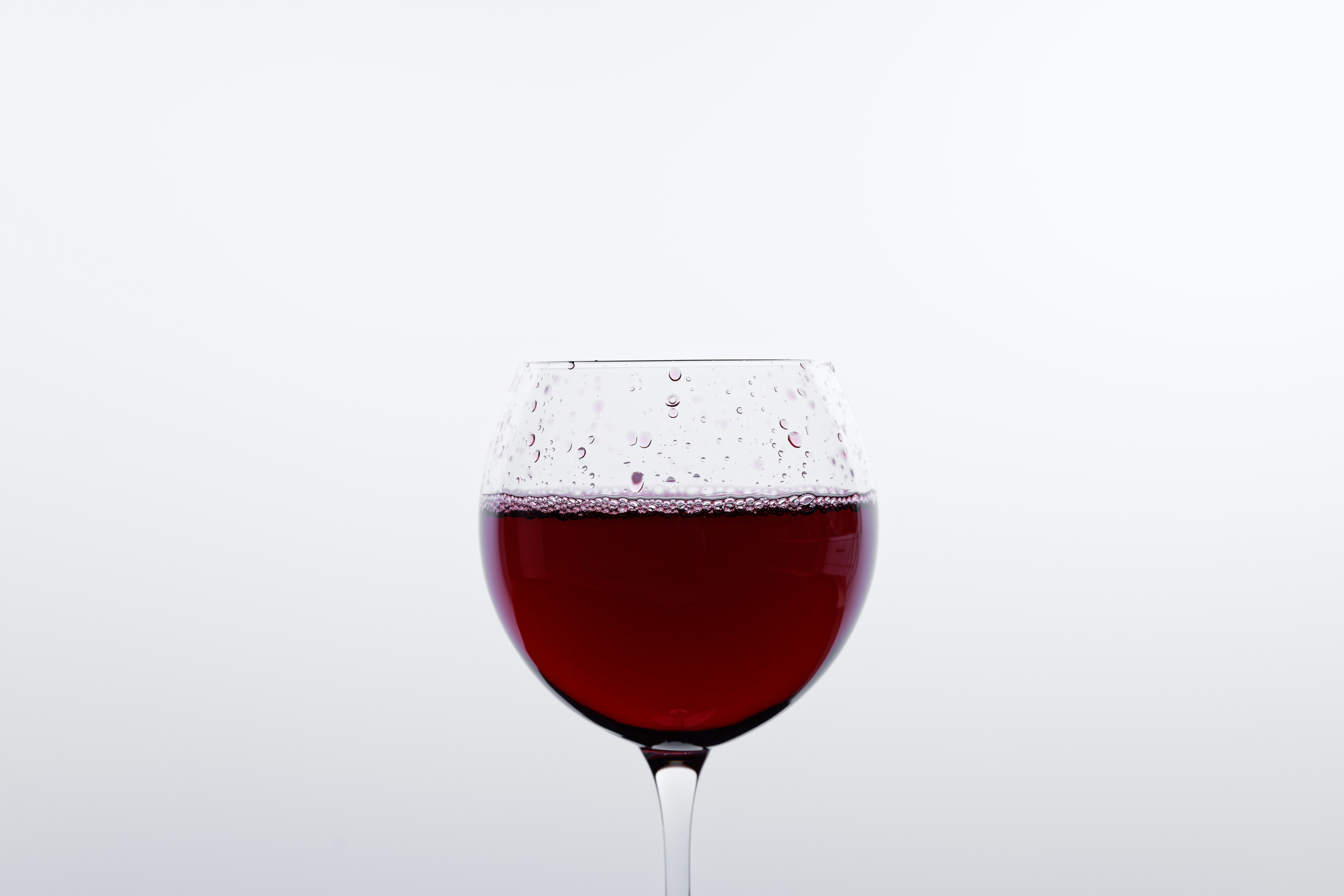clear wine glass with red liquid, a glass of red wine in front of a white background